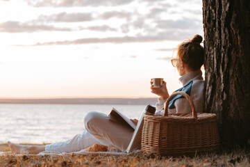 Woman drink tea or coffee from thermos read book having picnic at lake