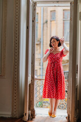 Fototapeta na wymiar a beautiful and happy brunette women in red retro dress in the balcony doorway 