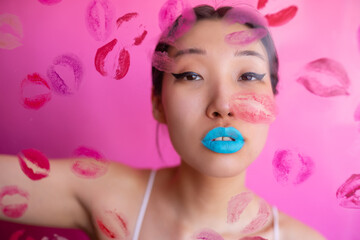 Woman with colorful makeup behind wall with kiss stains