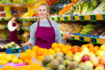 Happy woman store worker in apron at fruit department of supermarket