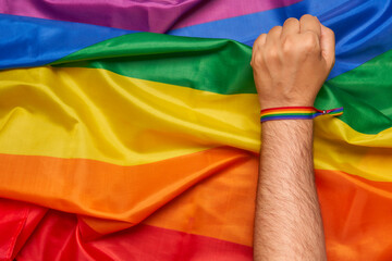 Activist's fist with LGBT wristband on rainbow flag background