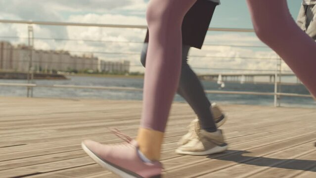 Low section of four unrecognizable male and female athletes jogging on promenade in cite at summertime