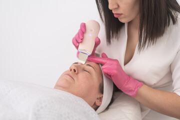 Obraz na płótnie Canvas middle age woman get a deeper clean with ultrasonic scrubbers and ultrasound face therapy. cosmetologist skill as they use apparatus for a professional facial cleansing. 