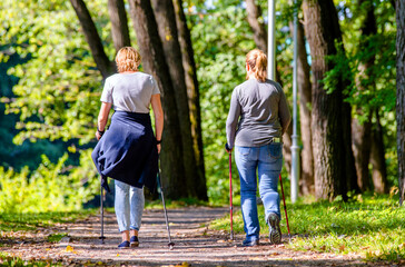 An elderly womans does Nordic walking in a city park
