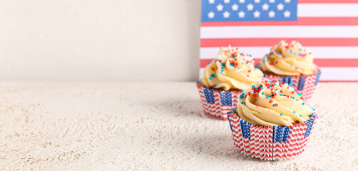 Fototapeta na wymiar Tasty patriotic cupcakes on light table against USA flag. Banner for American Independence Day