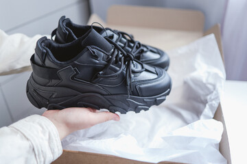 Unpacking women's shoes, stylish black sneakers in hands