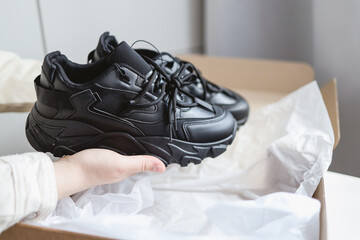 Unpacking women's shoes, stylish black sneakers in hands