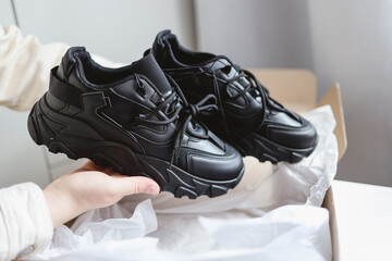 Unpacking women's shoes, stylish black sneakers in hands