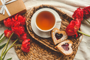 Tray with tasty breakfast, bouquet of peonies and gift for Valentine's Day on bed