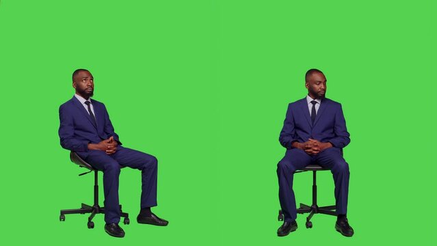 Male company entrepreneur sitting on chair in studio, wearing business suit and posing over full body green screen. Young office worker feeling confident on camera, corporate manager.