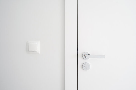 Closed door with metal handle and lock close to light switch on white wall