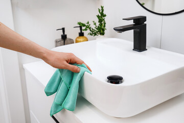 Woman cleaning white washbowl with a black tap in bathroom