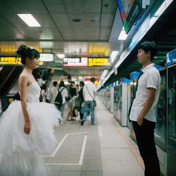 Couples in wedding dresses stand on the subway platform