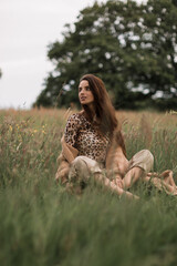 Young beautiful brunnet woman sitting on a green meadow, looking at camera. Summer outdoor