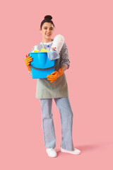 Young woman with cleaning supplies  on pink background