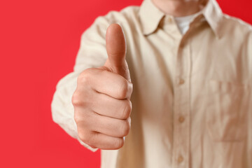 Young man showing thumb-up on red background