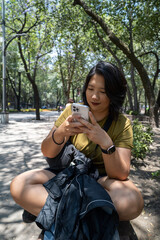 Portrait of Asian Woman happy using a Mobile Phone at the Park in Mexico City