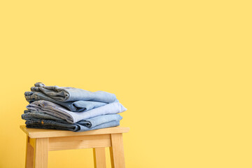 Stool with folded jeans on yellow background