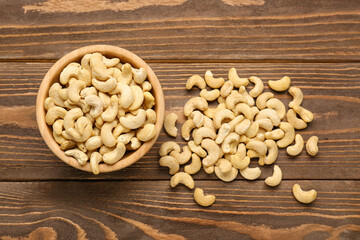 Bowl with tasty cashew nuts on wooden background