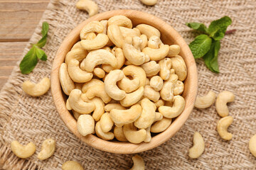 Bowl with tasty cashew nuts on wooden background