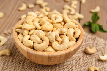 Bowl with tasty cashew nuts on wooden background