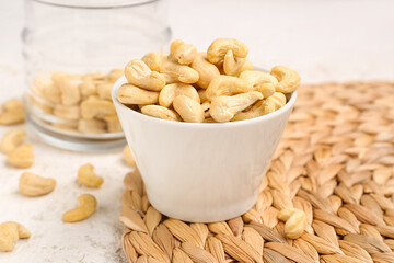 Bowl with tasty cashew nuts on light background