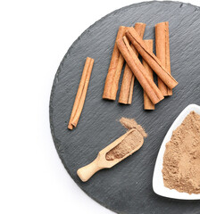 Slate board with cinnamon powder and sticks on white background, closeup