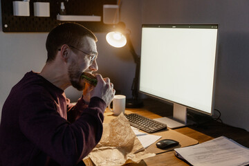 A man eats a sandwich while working in the office
