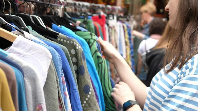 A young woman chooses clothes at the second-hand market. The concept of conscious consumption