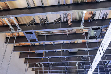Theater stage rigging with theatrical equipment, lighting, supports, and chains.  Photo taken from an elevated position looking across the rigging.