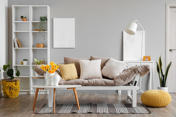 Interior of stylish living room with cozy sofa and blooming narcissus flowers on coffee table