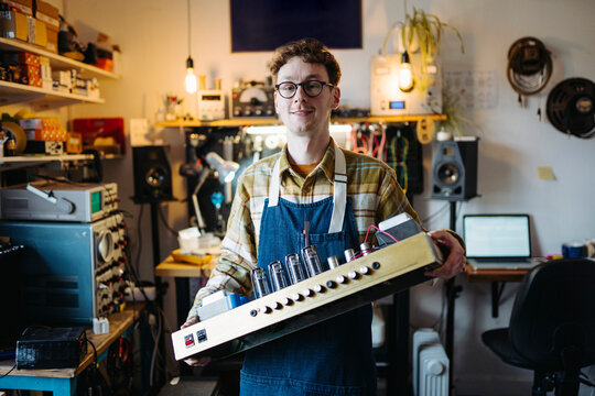 Smiling repairman holding valve guitar amplifier in workshop