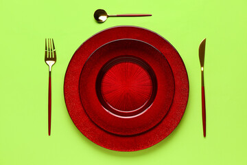 Table setting with clean plate and cutlery on green background