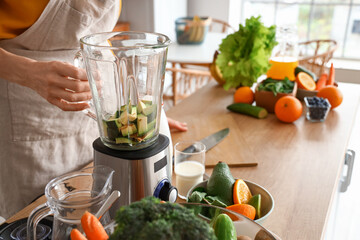 Mature woman with cut avocado making healthy smoothie in kitchen, closeup