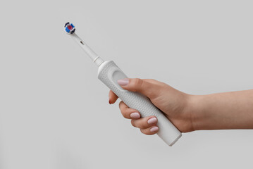 Female hand with electrical toothbrush on grey background