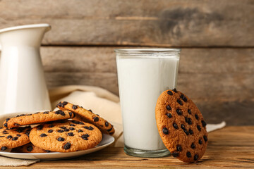 Tasty cookies with chocolate chips and glass of milk on wooden background