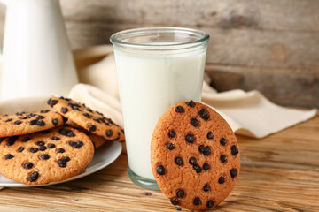 Tasty cookies with chocolate chips and glass of milk on wooden background
