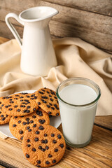 Tasty cookies with chocolate chips and glass of milk on wooden background