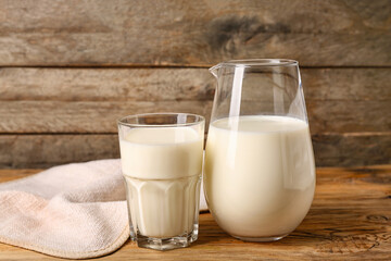Jug and glass of fresh milk on wooden background