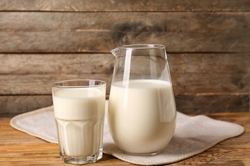 Jug and glass of fresh milk on wooden background