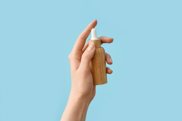 Hand holding bottle with cosmetic serum on light blue background