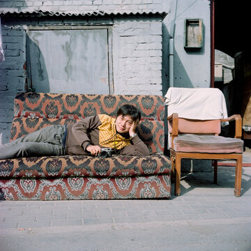 The man is lying on the old sofa with a camera on his side