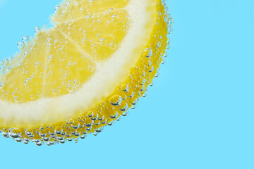 Lemon slice in water with bubbles on blue background