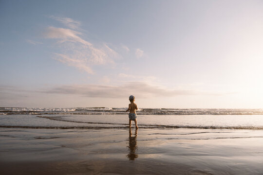 Toddler walks to calm beach at sunset.