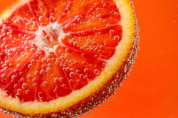 Blood orange slice in water with bubbles on red background