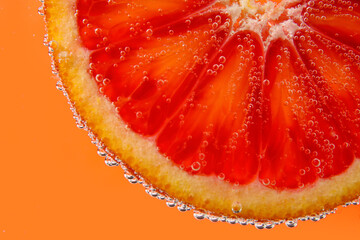 Blood orange slice in water with bubbles on red background