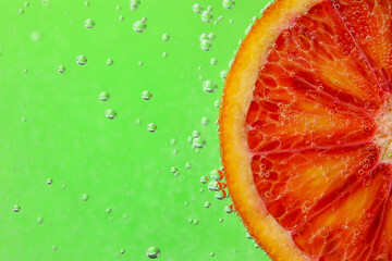 Blood orange slice in water with bubbles on green background