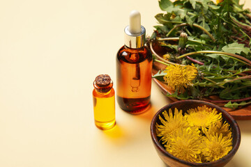 Bottles with cosmetic oil and plate of dandelion flowers on beige background