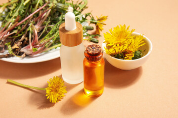 Bottles with cosmetic oil and plate of dandelion flowers on orange background