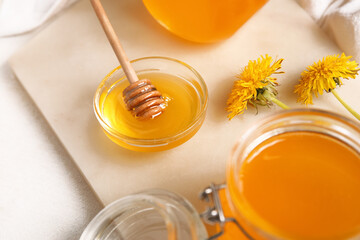 Board, jars and bowl with dandelion honey on white background